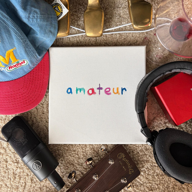 The amateur album cover: a white canvas reading “amateur” in crayon, surrounded by a cap, headphones, a microphone, a guitar headstock and a glass of red wine